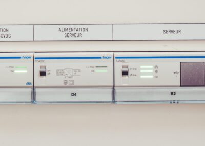 Gros plan sur un tableau de contrôle de gestion technique du bâtiment (GTB) ou de domotique, intégré dans une installation électrique. Les modules sont des équipements professionnels (marques Hager et Siemens) identifiés par des étiquettes : "ALIMENTATION BUS KNX 30VDC", "ALIMENTATION SERVEUR" et "SERVEUR". Des voyants verts et rouges ("OK", "Bus OK") indiquent l'état de fonctionnement des différents circuits.