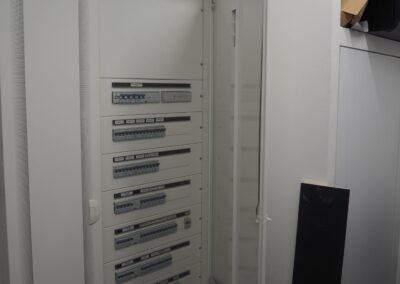 Armoire électrique ouverte dans une pièce technique, montrant plusieurs rangées de disjoncteurs et d’équipements de contrôle.