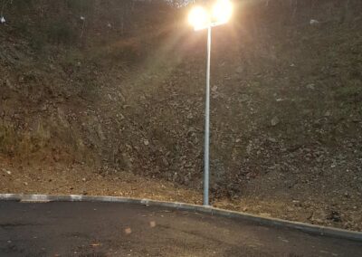 Un mât d'éclairage extérieur est allumé au crépuscule. La lumière vive émise par le double projecteur éclaire la nouvelle surface de bitume