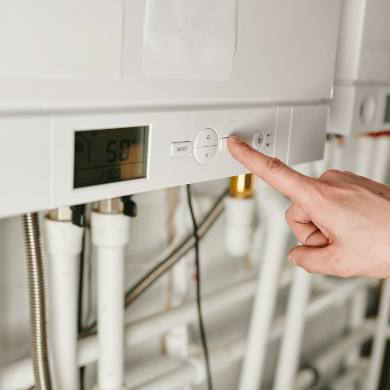 Une main ajuste les paramètres sur le panneau de contrôle numérique d'une chaudière murale blanche. L'écran affiche 50 degrés.