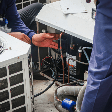 Un technicien en tenue de travail inspecte les composants internes et le câblage d'une unité de climatisation extérieure ouverte.