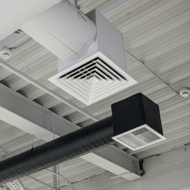 Plafond industriel avec des conduits de ventilation apparents et des diffuseurs d'air carrés de couleurs blanche et noire.