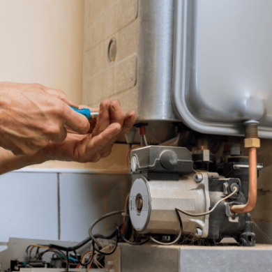 Vue rapprochée d'un technicien utilisant un tournevis pour intervenir sur le circulateur d'une chaudière ouverte, montrant les composants hydrauliques et électriques.