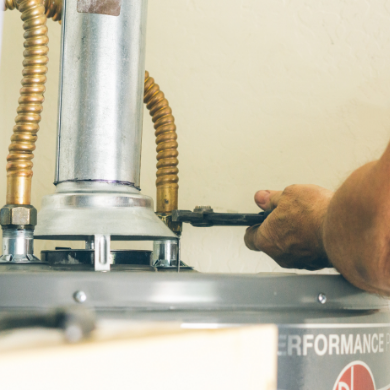 Vue rapprochée d'un artisan plombier utilisant une clé pour intervenir sur les raccords supérieurs d'un chauffe-eau. On distingue les tuyaux d'alimentation flexibles et le conduit d'évacuation métallique sur le dessus de l'appareil.