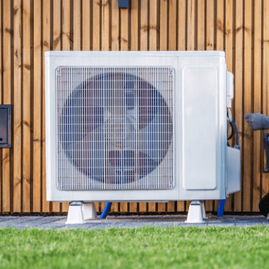 Vue de face d'une unité extérieure de pompe à chaleur blanche installée sur des supports au sol, devant un bardage en bois naturel et une pelouse verte.