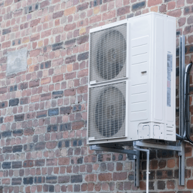 Une grande unité extérieure de pompe à chaleur blanche avec deux ventilateurs, installée en hauteur sur un support métallique robuste contre un mur en briques rouges.